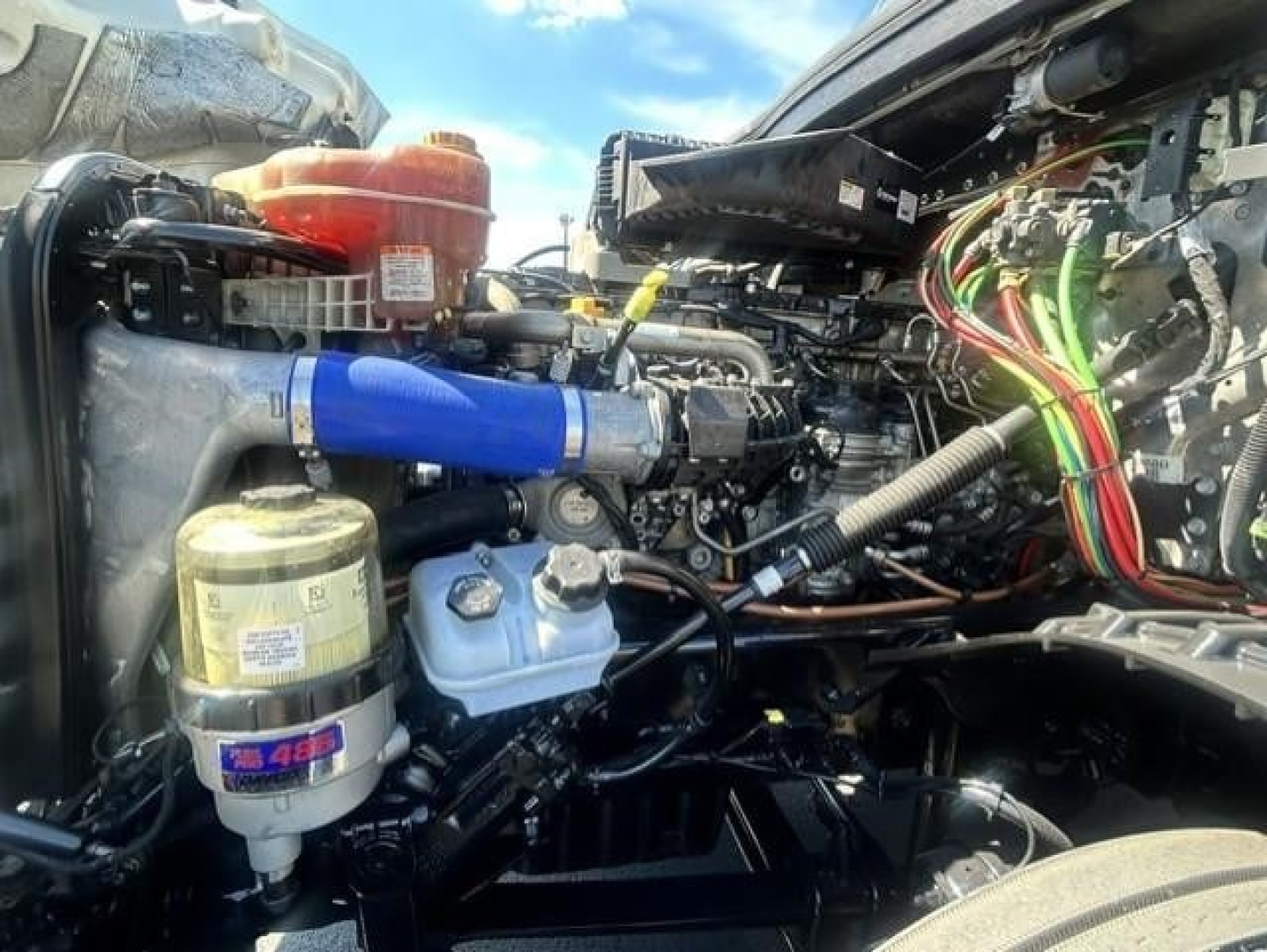 Fleet truck engine bay showing filter canister, blue silicone hose, coolant reservoir, air intake, and wiring harness in Freightliner Cascadia engine bay.