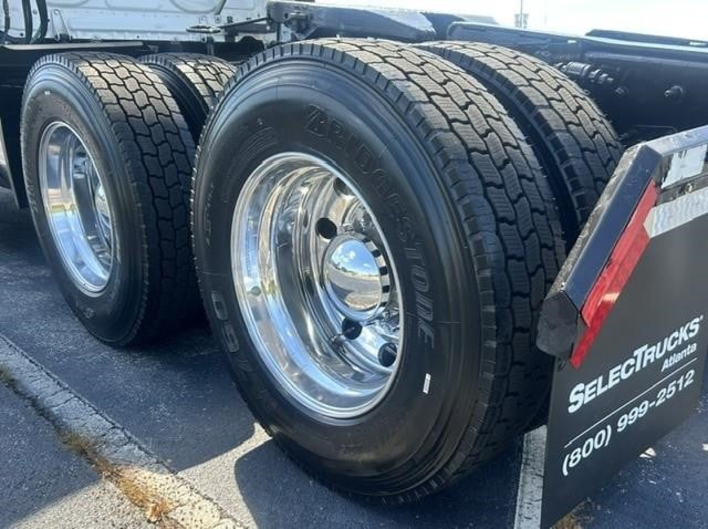 Rear triple axle trucks with large dual tires and shiny chrome wheels in a freightliner Cascadia day cab.