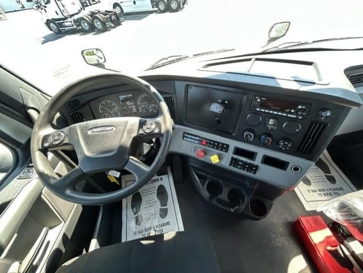 Cab interior of a Freightliner Cascadia truck shows steering wheel, dashboard with gauges, controls, and center console.