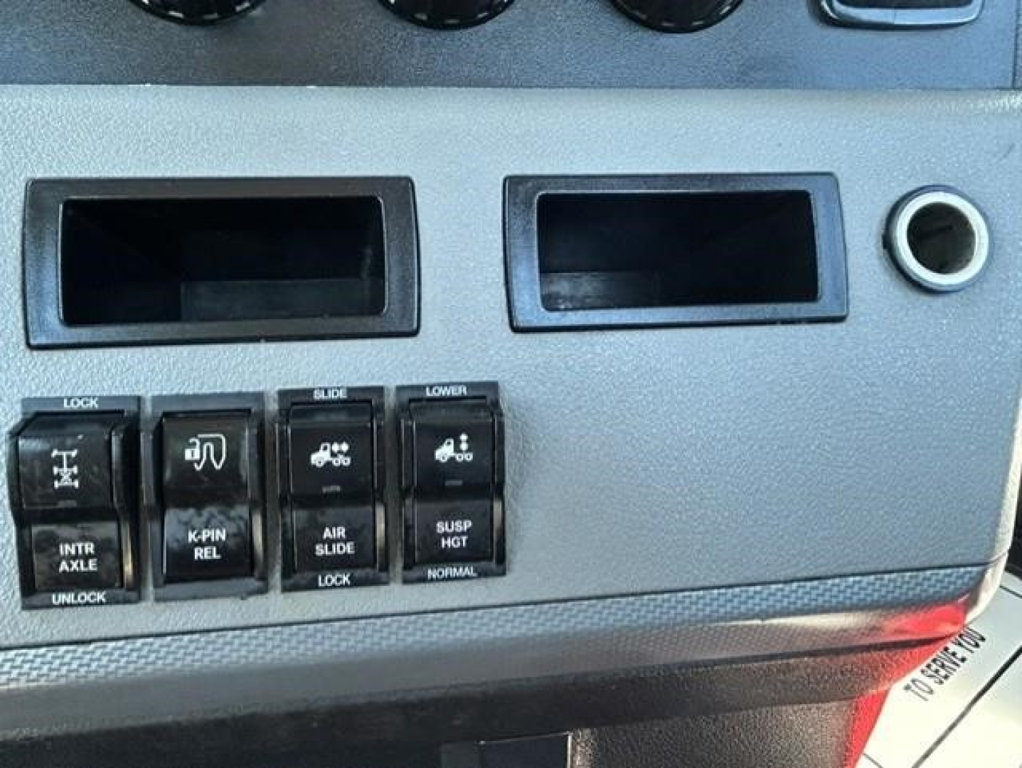 Dashboard switch panel with multiple labeled switches and two empty display slots. Visible text on switches includes LOCK, INTR AXLE, K-PIN REL, AIR SLIDE, SUSP. HGT, LOWER, U NLOCK, and icons.