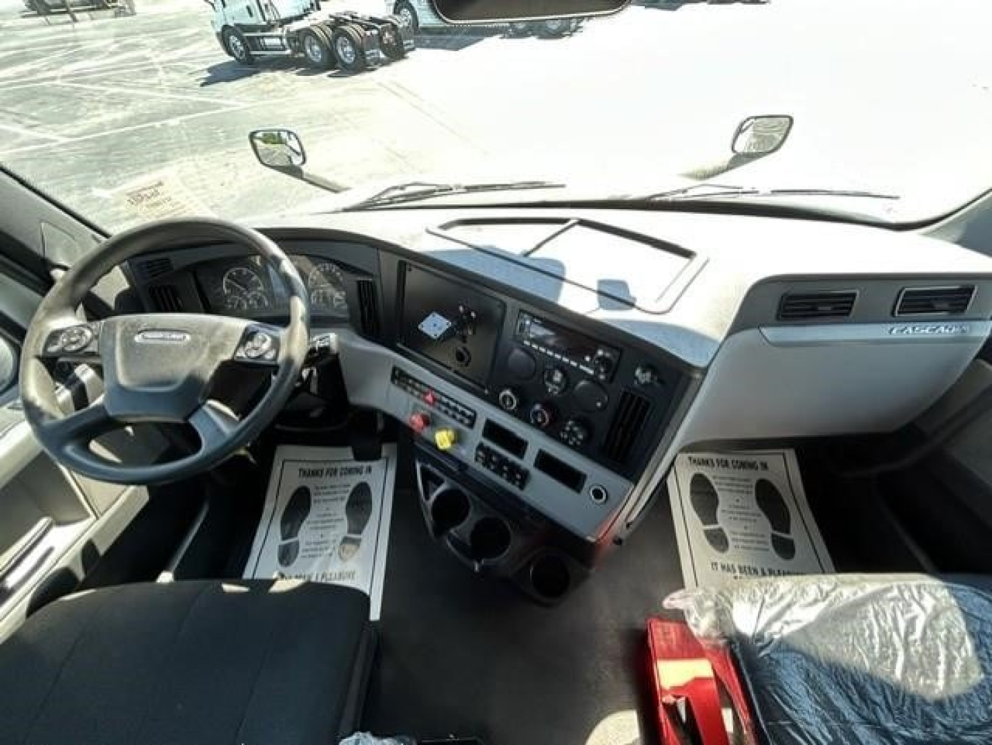 Interior of a Freightliner Cascadia 126 cab showing steering wheel, dashboard, center console, and driver and passenger seats.