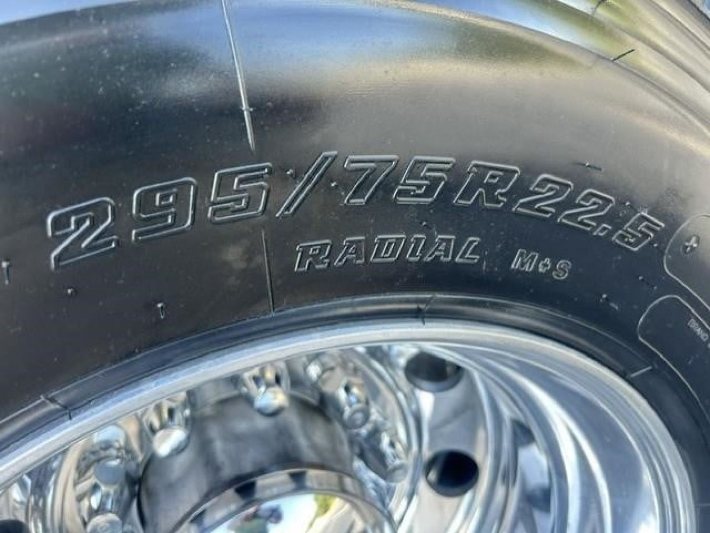Tire with embossed markings showing 295/75R22.5 RADIAL M+S on the sidewall and a polished steel wheel.