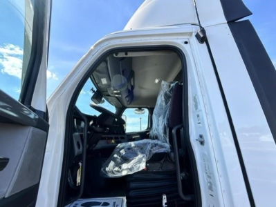 Truck cab interior of a 2022 Freightliner Cascadia 126 Day Cab showing open driver door, steering wheel, seat with plastic cover, and dashboard.