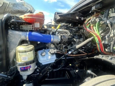 Fleet truck engine bay showing filter canister, blue silicone hose, coolant reservoir, air intake, and wiring harness in Freightliner Cascadia engine bay.