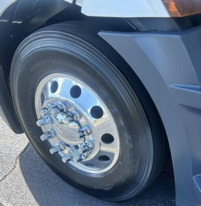Front wheel of a 2022 Freightliner Cascadia 126 day cab showing polished steel wheel with chrome hub and lug nuts, tire and fender visible.