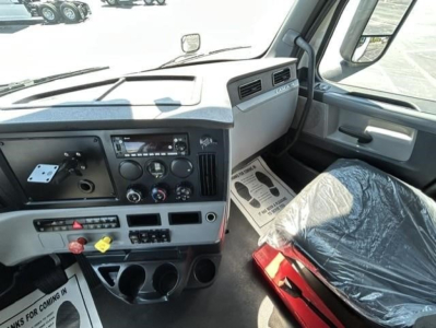 Freightliner Cascadia 126 truck interior dashboard view showing steering wheel, instrument cluster, center console, and driver seat wrapped in protective plastic.
