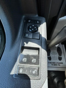 Seat panel with window and mirror controls in a Freightliner Cascadia interior; visible buttons include window switch, mirror selector, and locking switch.