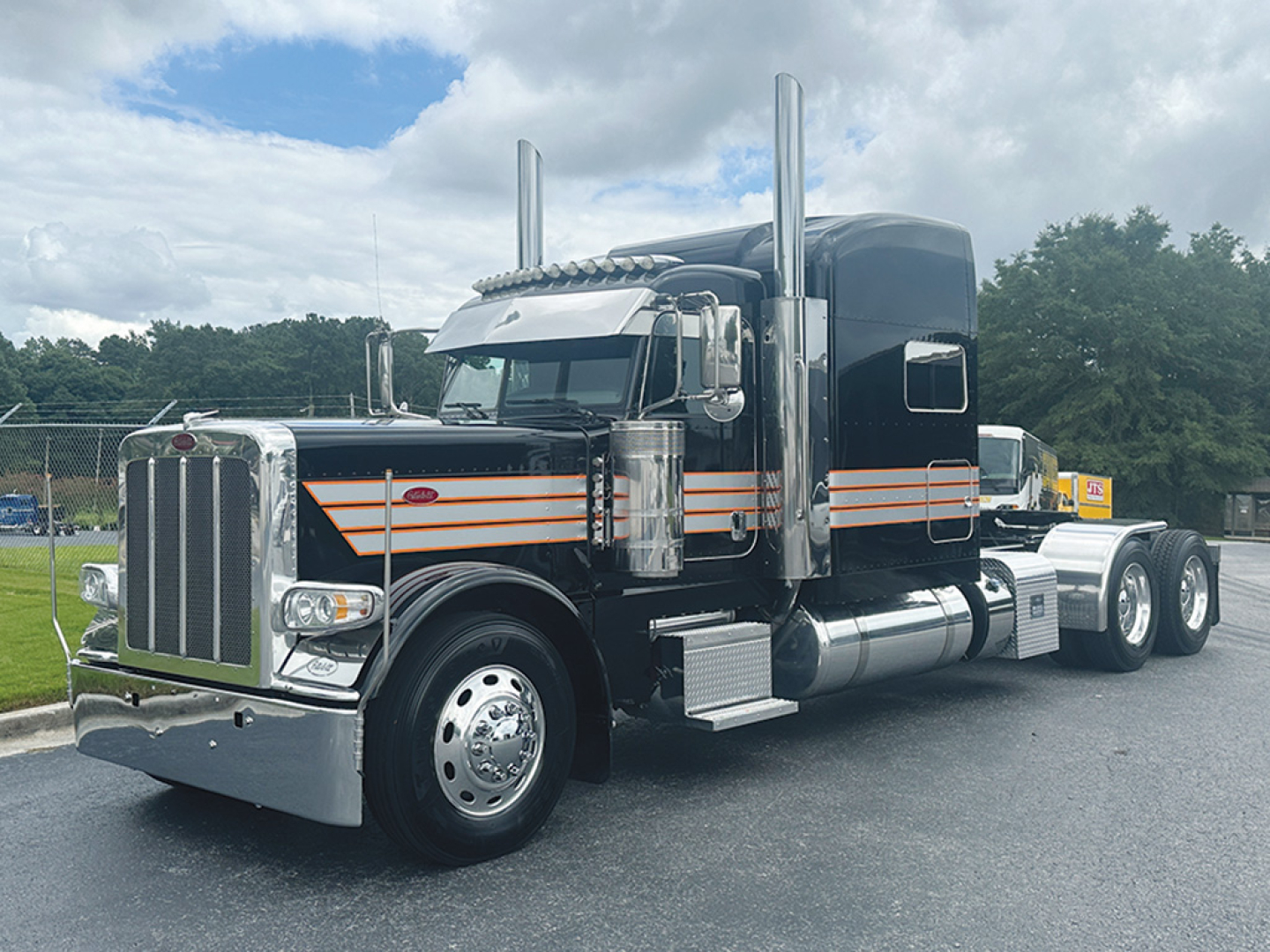 Peterbilt 389 tractor unit in black with orange pinstriping, chrome accents, and tall exhaust stacks, front grille, and dual rear axles.