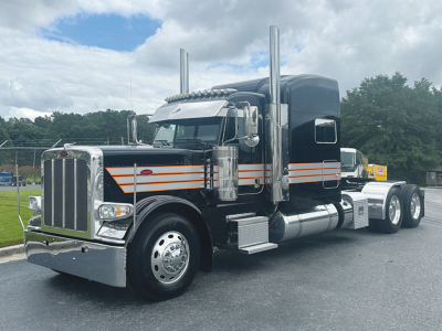 Peterbilt 389 tractor unit in black with orange pinstriping, chrome accents, and tall exhaust stacks, front grille, and dual rear axles.