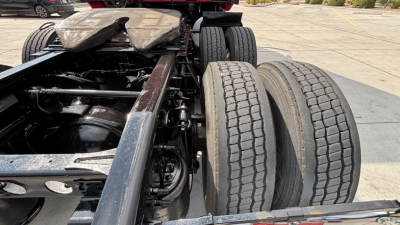Tractor-trailer chassis view showing tandem rear axles and dual tires under the frame, with visible suspension components and drivetrain area.