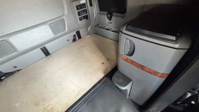 Truck cab interior showing a wooden sleeper bunk platform in a 2022 International LT625 sleeper cab. Center console and storage area visible.