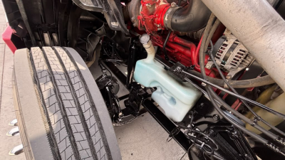 Truck undercarriage view showing front suspension, steering linkage, and coolant reservoir with light blue translucent cap.