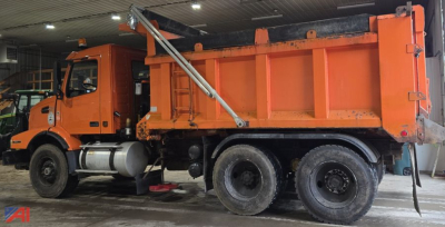 Volvo dump truck in-service showing orange dump bed and side view with cab and dual rear axles.