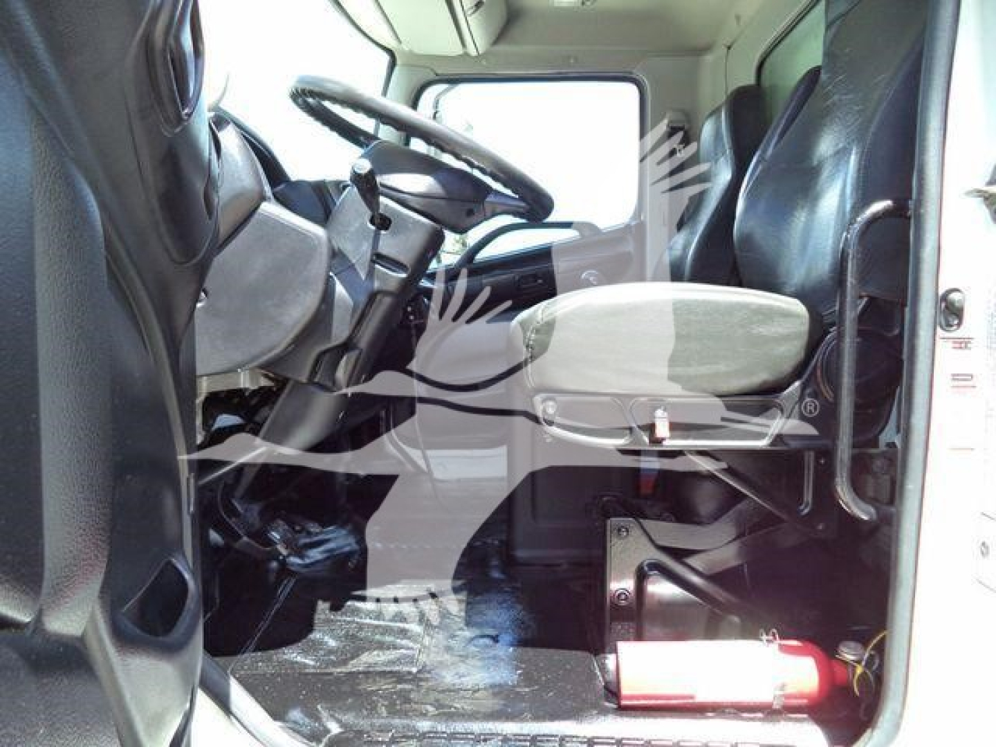 Cab interior of a 2015 Hino 268A with steering wheel, driver seat, and a fire extinguisher mounted behind the front bench.
