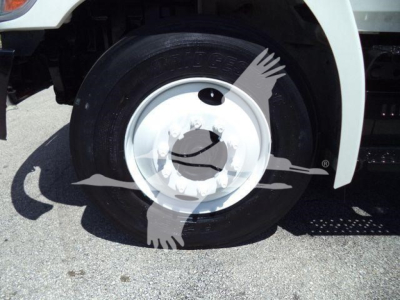 Front wheel and tire of a 2015 Hino 268A refrigerated truck showing steel wheel with hubcap and fender, part of truck chassis.