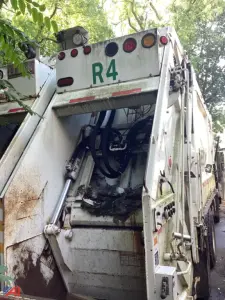 Crane Carrier low entry cab over engine rear showing hydraulic hoses and compactor body with 'R4' marking.