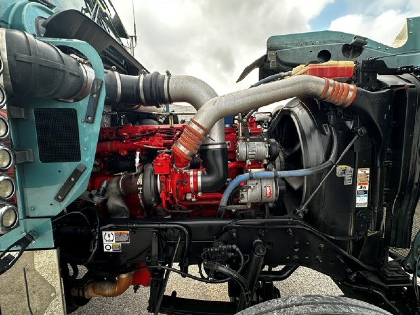Kenworth W900L engine bay showing red diesel engine with intake piping and surrounding components.