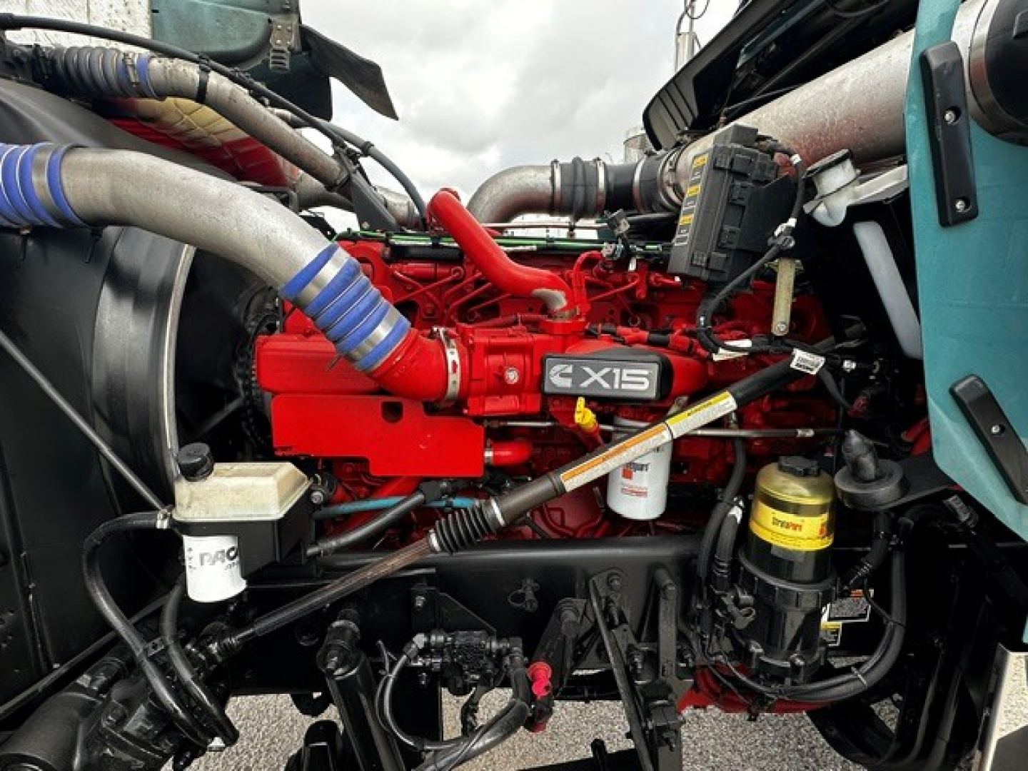 Kenworth W900L engine bay showing red 4X15 engine block with various hoses, filters, and an oil reservoir visible.