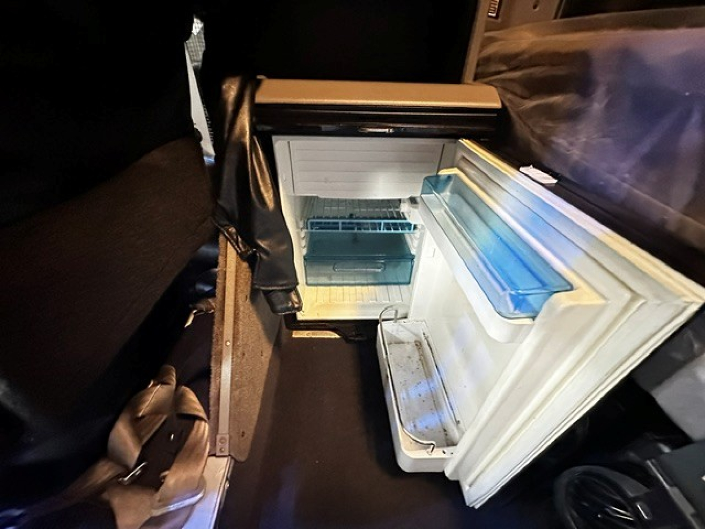 Cab interior showing a small under-dash refrigerator/freezer with open door, light interior, and blue ice-pack shelves.
