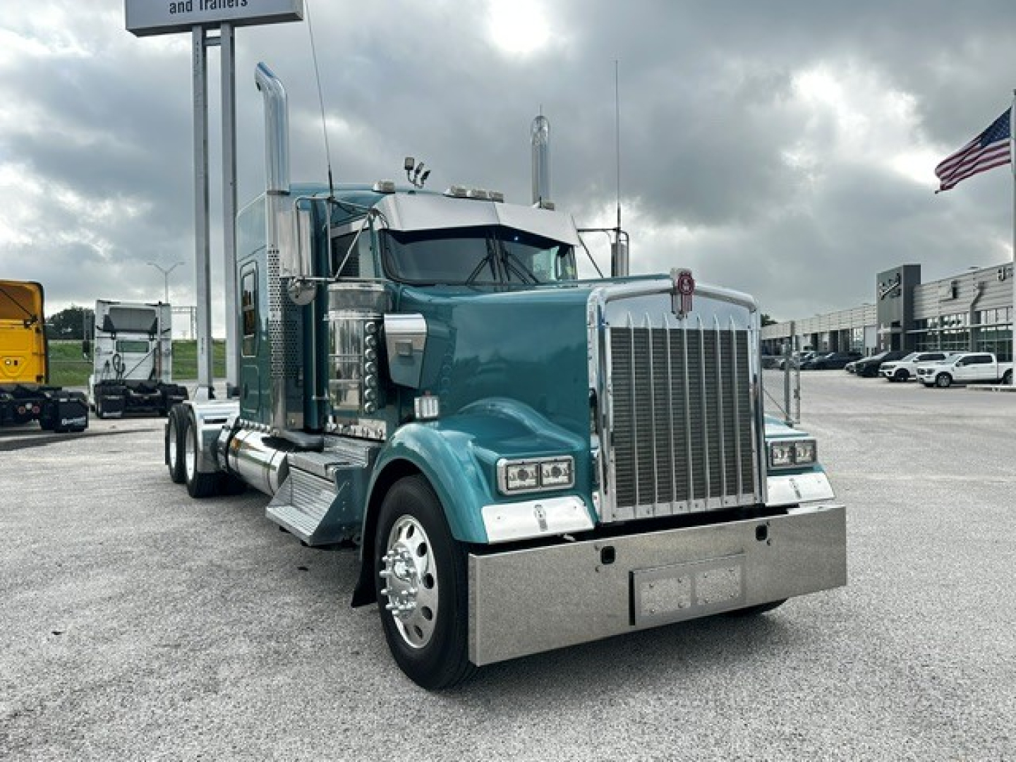 Kenworth W900L truck in teal with chrome grille and bumper, front view, twin exhaust stacks, daytime outdoor lot