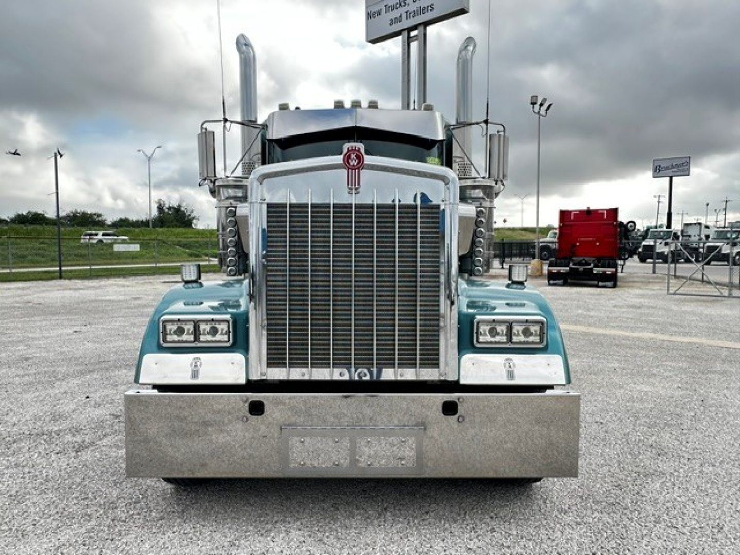 Kenworth W900L truck front view showing large chrome grille, upright exhaust stacks, dual rectangular headlights, and metal bumper.