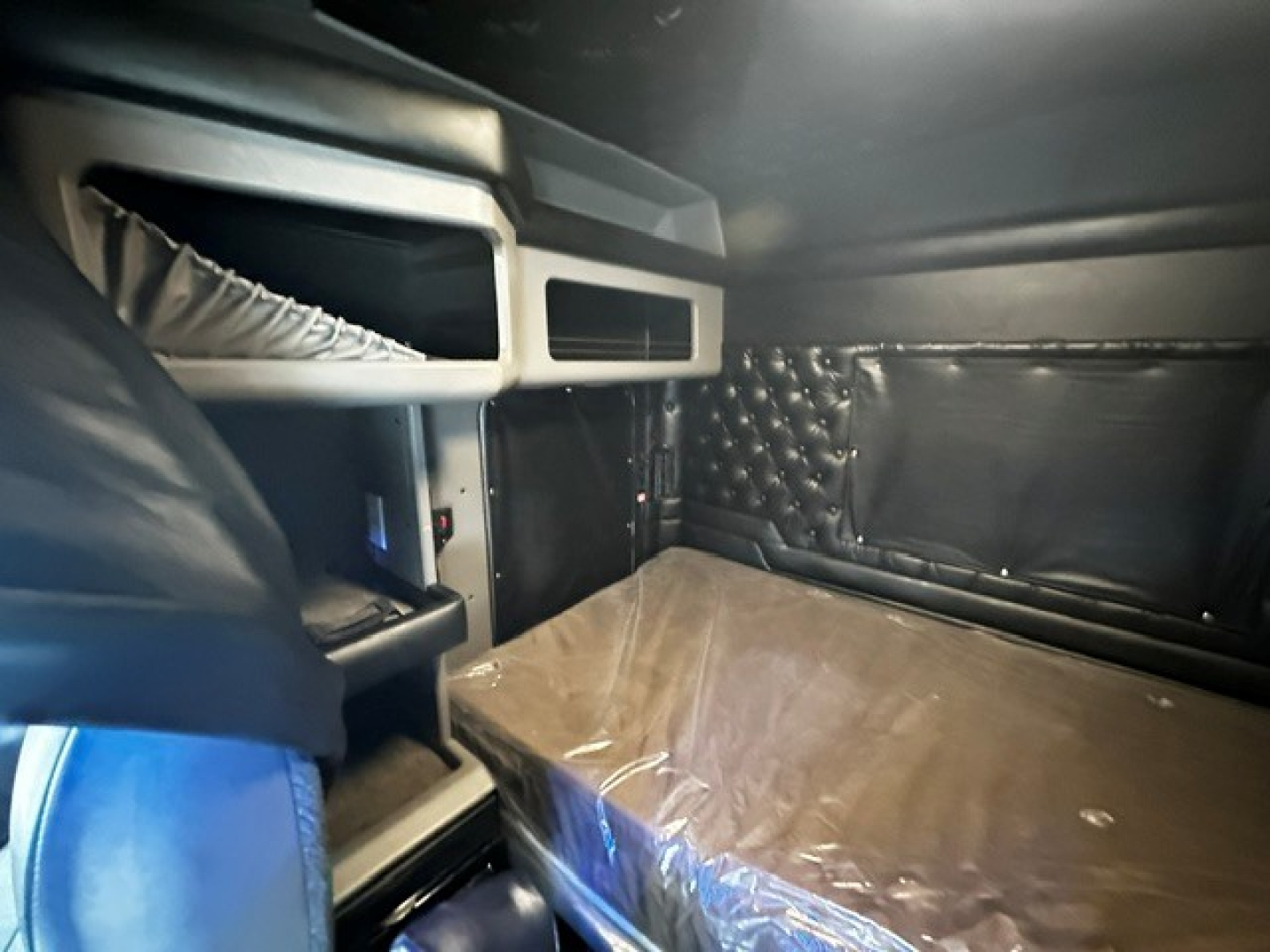 Kenworth W900L interior cab area showing sleeper bed with plastic cover, side storage, and dashboard panels visible.