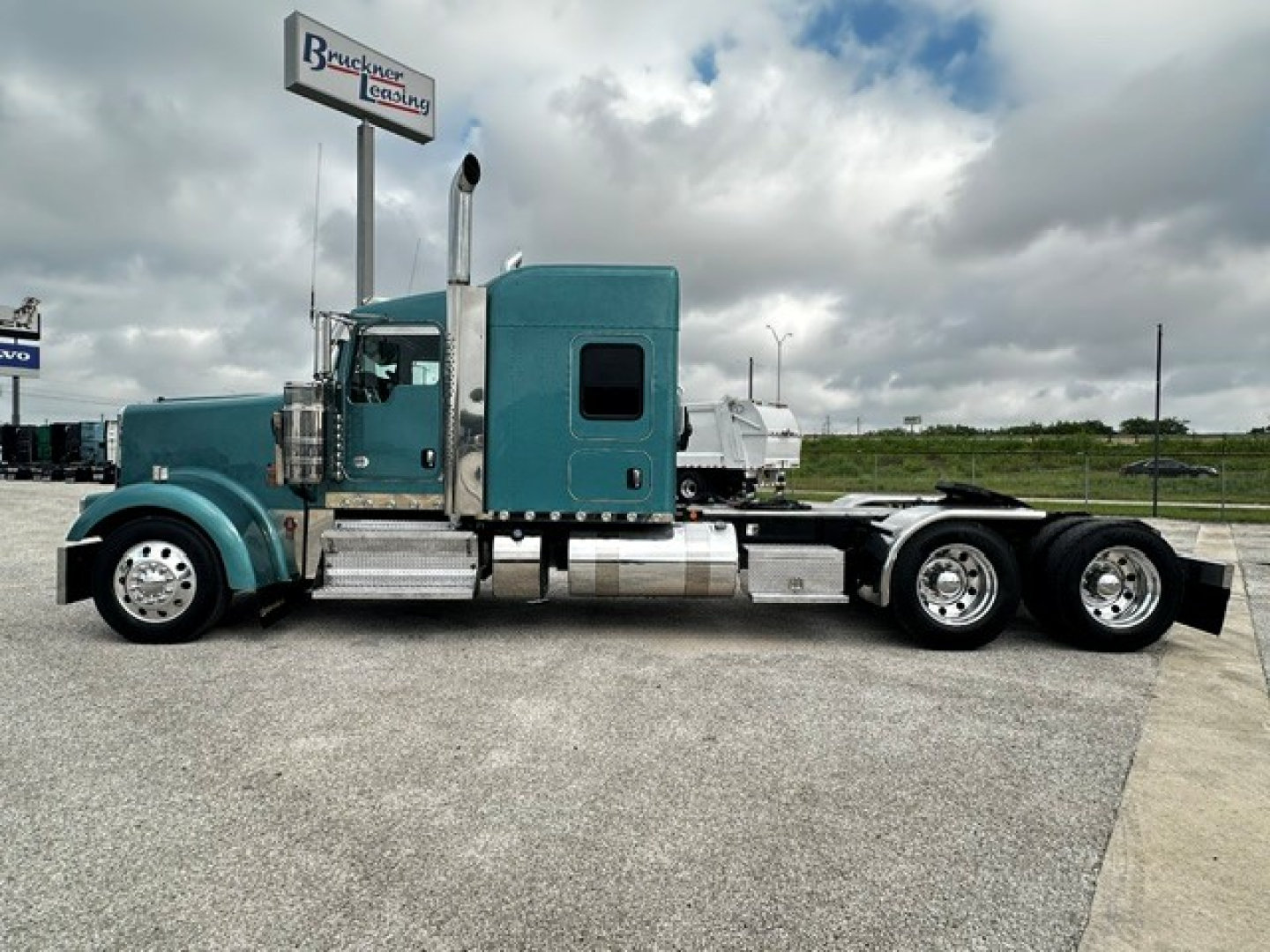 Kenworth W900L tractor-trailer in teal showing side profile with sleeper cab and dual rear axles.