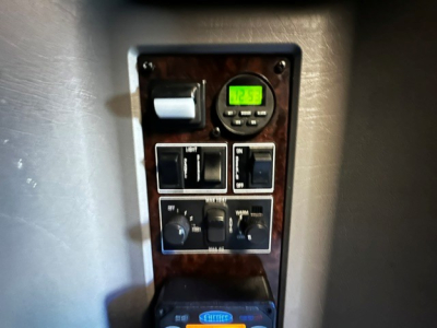 Kenworth W900L interior control panel with switches and a small digital display showing 12.5.6? The image shows a panel with a switch bank, gauge, and two toggle switches; woodgrain panel.