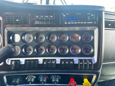 Kenworth W900L dash cluster and controls showing multiple round gauges and switch panels in a truck interior.