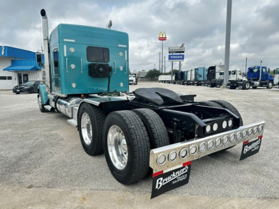 Kenworth W900L tractor rear view showing dual rear axles, turquoise sleeper cab, chrome fuel tanks, and polished tandem with bumper guard.