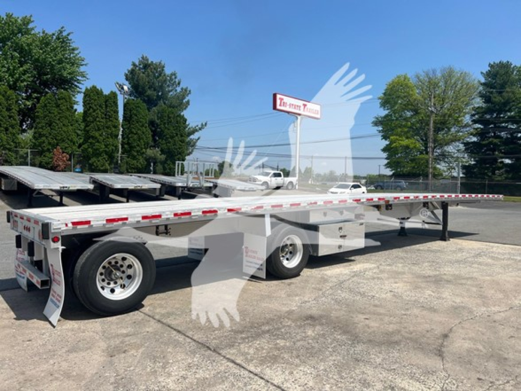 Flatbed trailer showing dual rear axles with compact wheel wells and white reflective tape, 2015 Reitnouer Maxmiser, VIN 1RNF48A26FR032305.