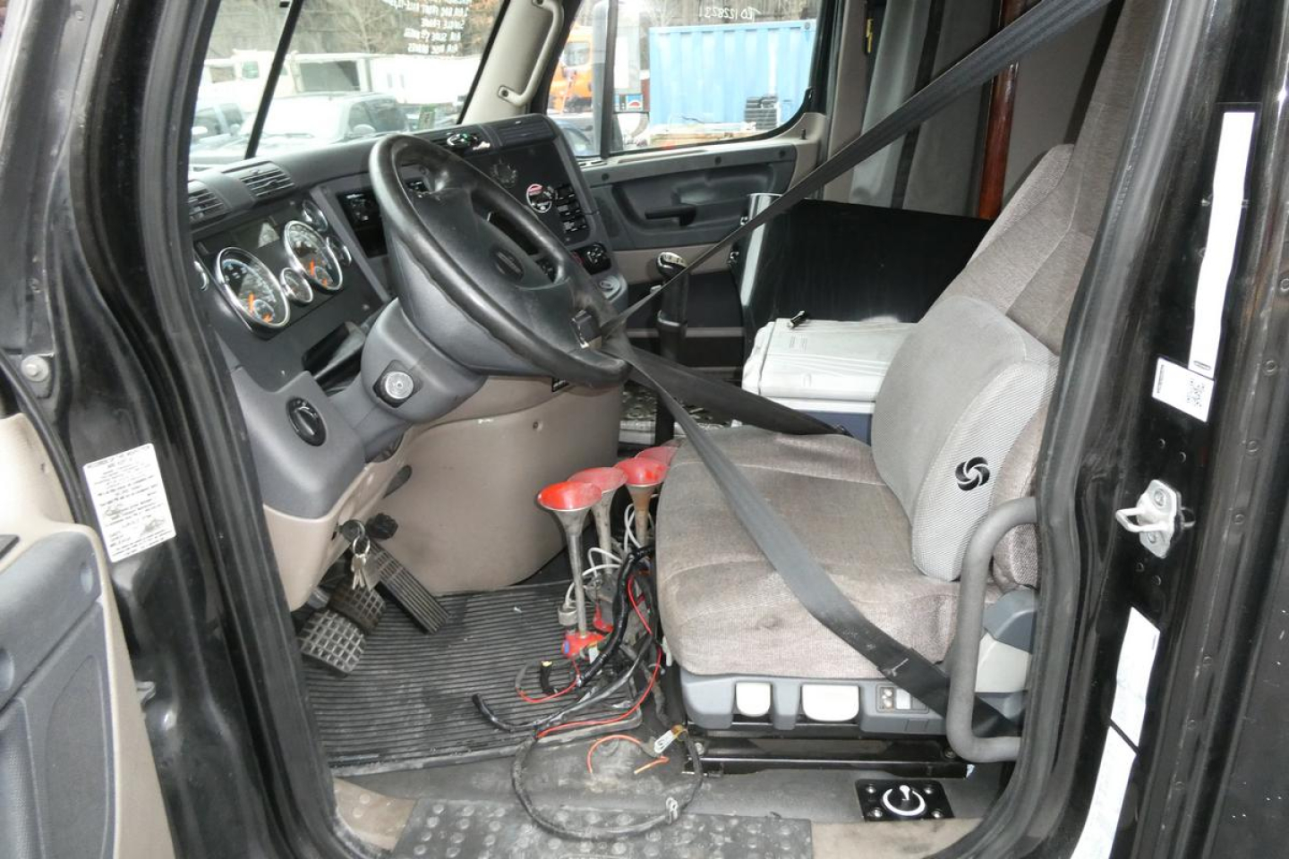 Cab interior of a Freightliner Cascadia 125 truck showing steering wheel, dashboard, seats, and wiring near floor.