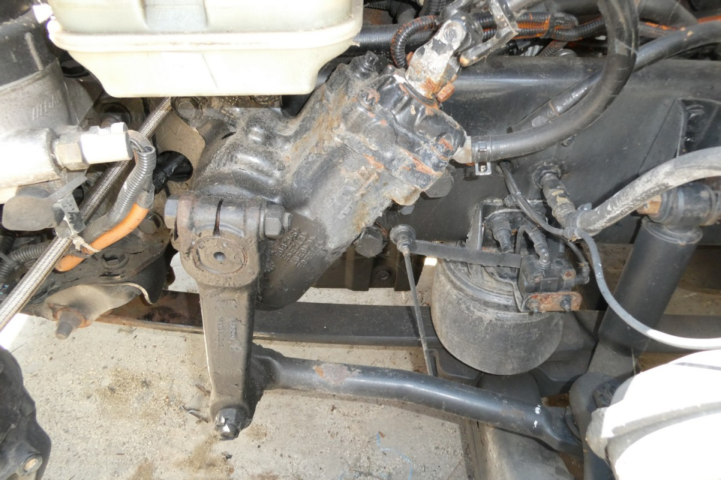 Front view of a Freightliner Cascadia 125 engine bay showing hydraulic lines, hoses, and componentry with a dusty steering/drive assembly.