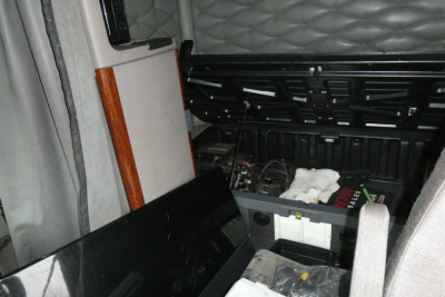 Cab interior of a Freightliner Cascadia 125 truck showing a storage area and electrical components under a side console.