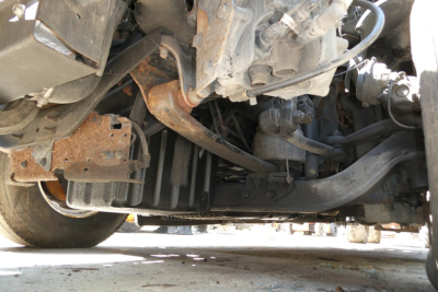 Underbody view of a Freightliner Cascadia 125 showing engine cradle, suspension, and radiator area with rusted brackets and hoses.