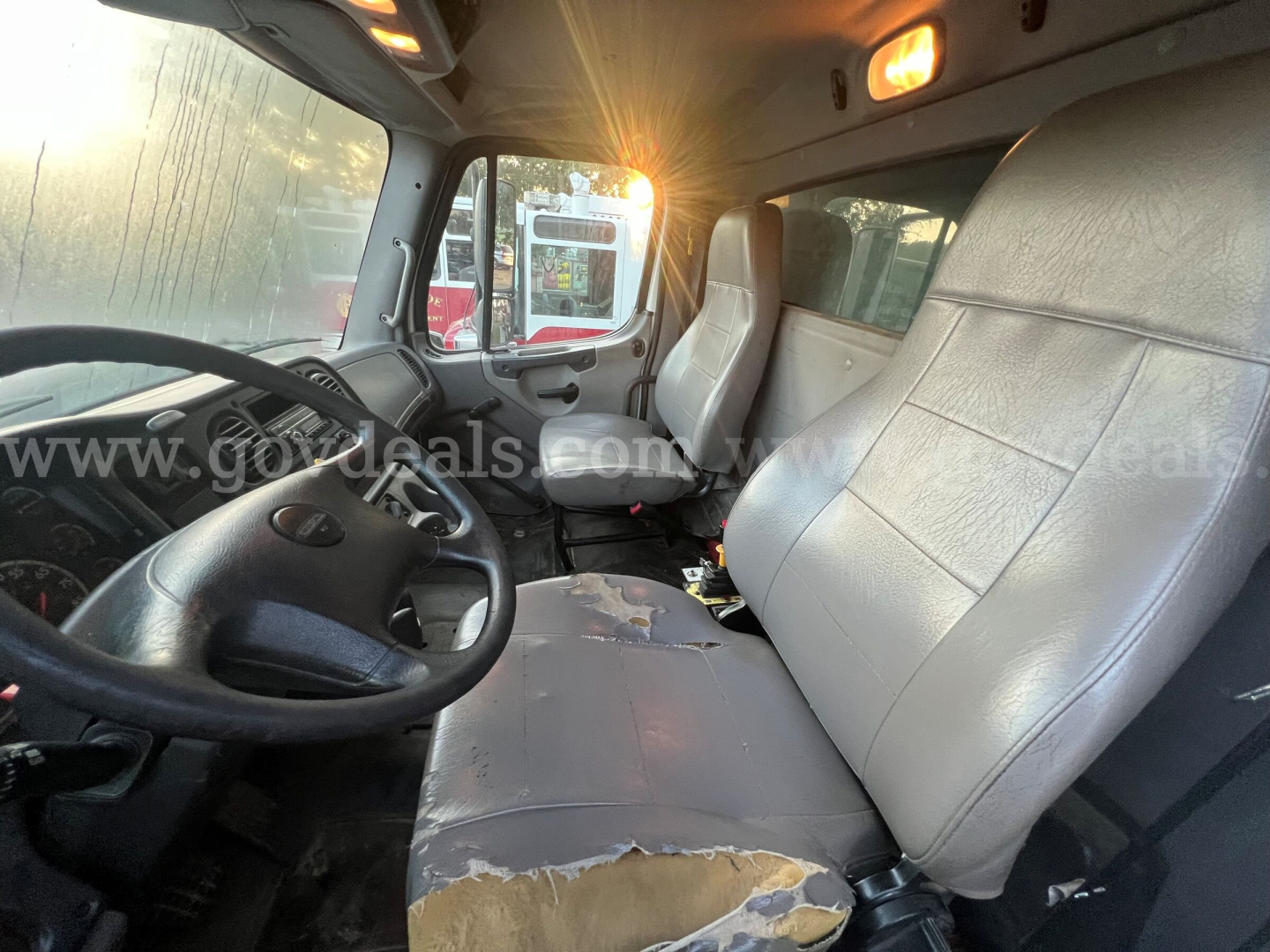Cab interior of 2017 Freightliner 114SD dump truck showing steering wheel, driver's seat, and worn center seat with torn upholstery.