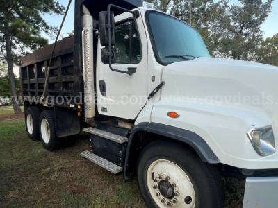 Freightliner 114SD dump truck side view showing cab, dual rear axles, and open-top dump bed with steps and large mirrors.