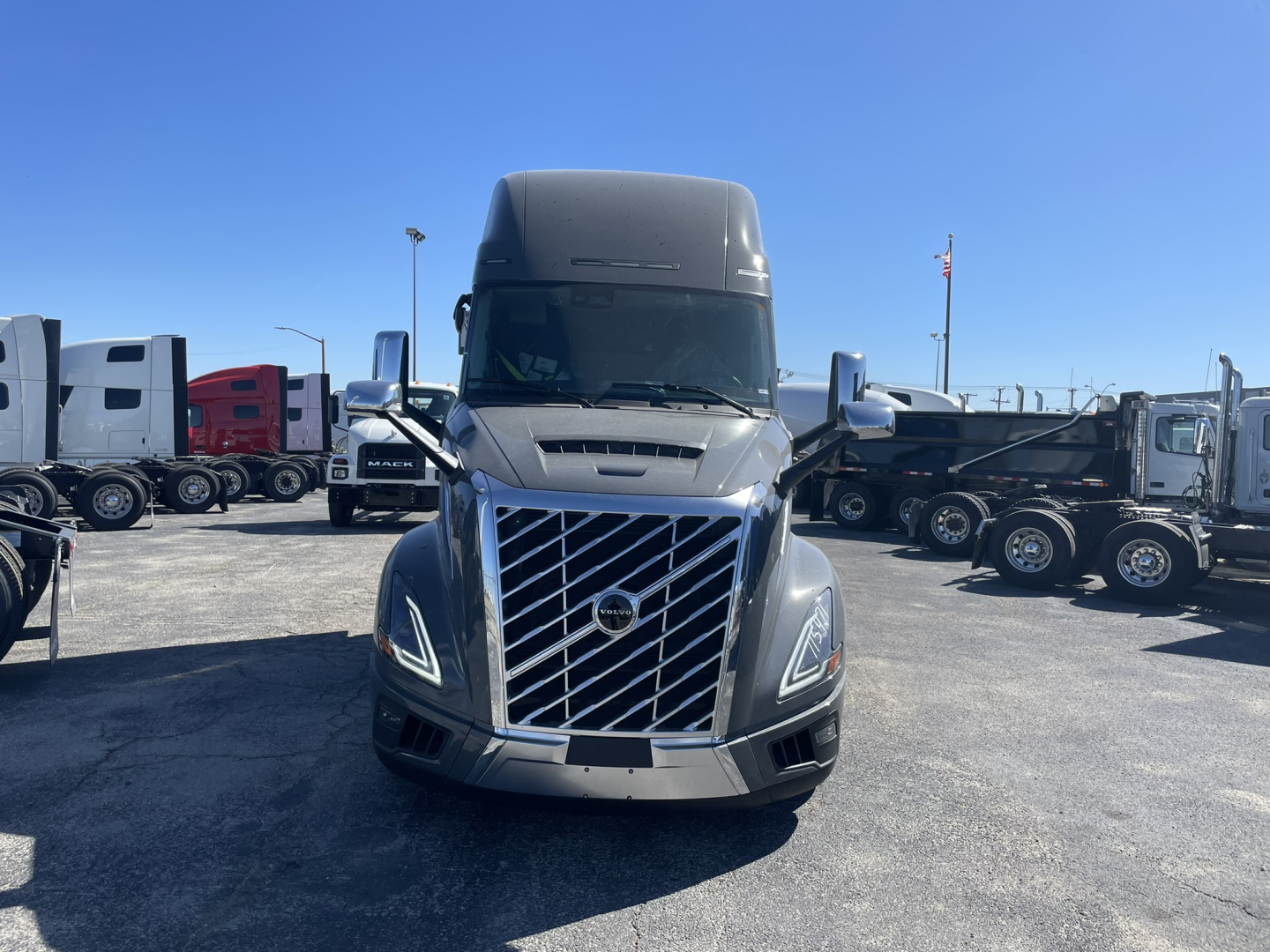 Volvo VNL64T860 truck cab front view showing chrome grille with Volvo emblem and headlights, fleet yard with other trucks in background.