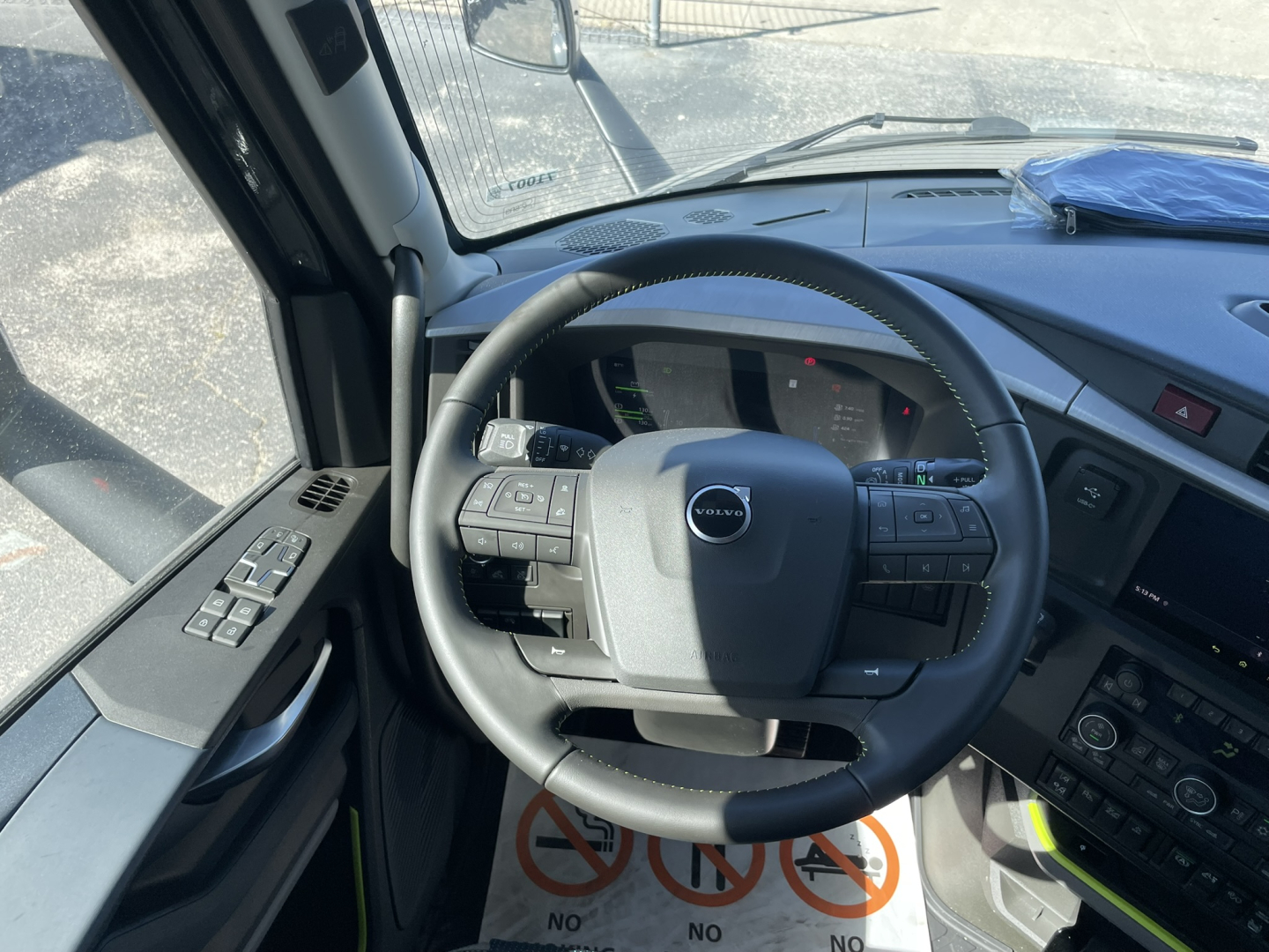 Volvo VNL64T860 truck interior view showing steering wheel and dashboard with control buttons on left and right; windshield and driver door window visible.