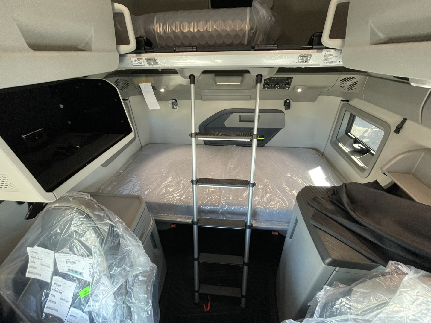 Volvo VNL sleeper cab interior with bunk bed and ladder, plastic-wrapped seats visible.