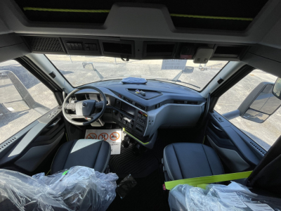 Truck cab interior showing dashboard and steering wheel with warning labels on the column; seats in view.