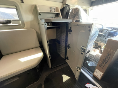 Volvo VNL64T860 truck interior showing an open cabinet under the sleeper with a metal shelf and wiring; driver seat and dashboard visible in background.