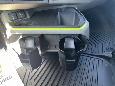 Two cup holders in the Volvo VNL64T860 interior with rubber floor mats and a small storage tray; illuminated lime-green accent line above cup holders.