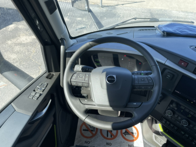 Volvo VNL64T860 truck interior view showing steering wheel and dashboard with control buttons on left and right; windshield and driver door window visible.