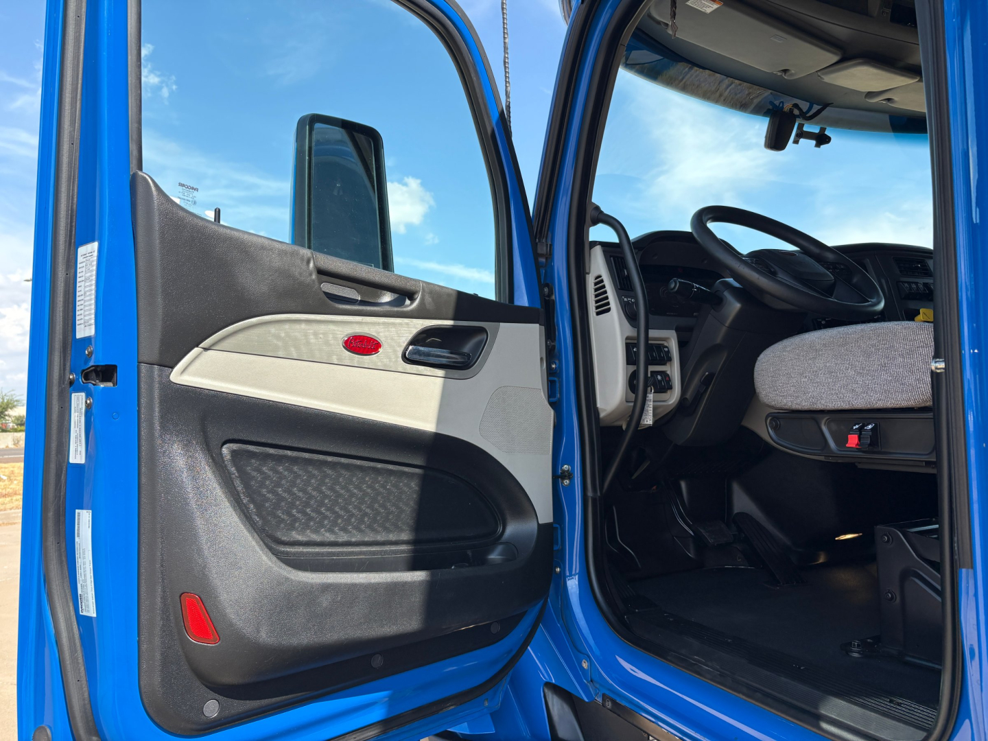 Truck cab interior view from open driver's door showing steering wheel and dashboard in blue Peterbilt 579.