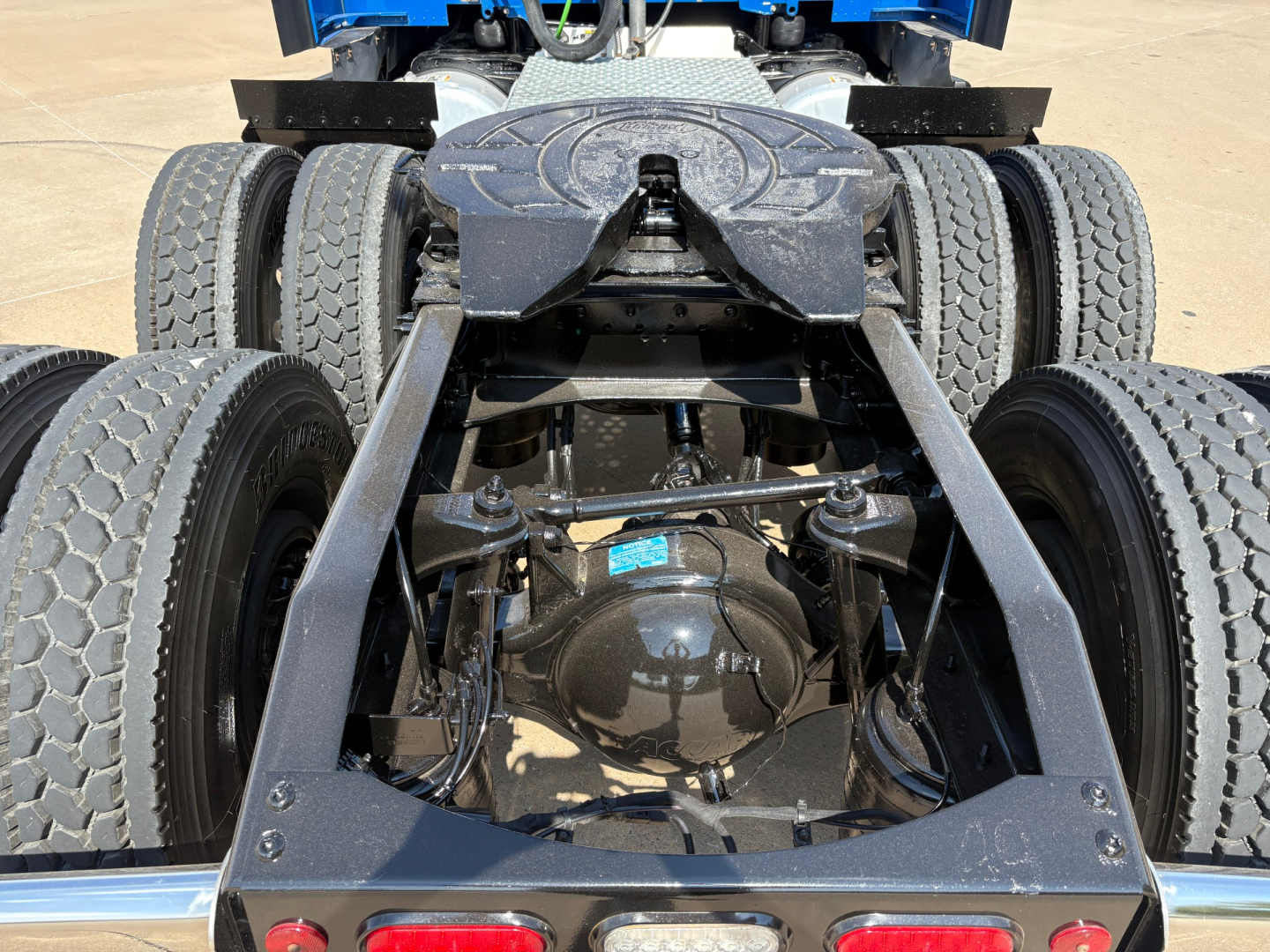 Dual rear axles of a Peterbilt 579 tractor showing the differential housing and suspension. View from behind the cab with fifth wheel area and frame rails visible.