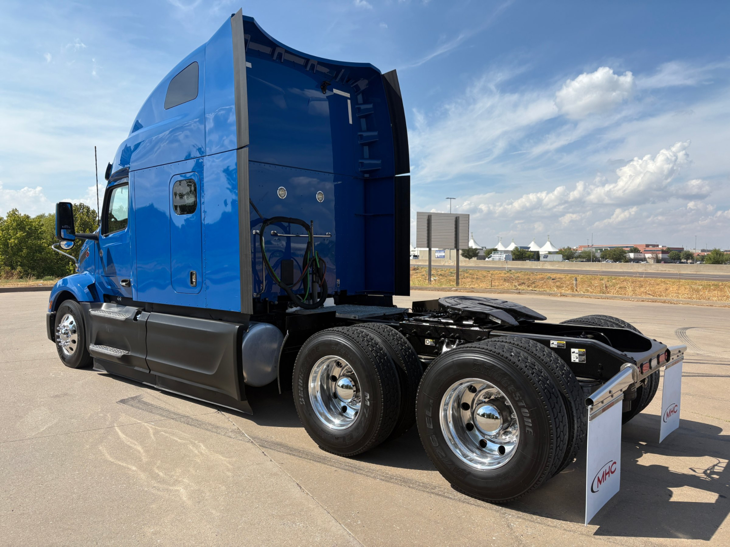 Peterbilt 579 sleeper tractor in blue, side view showing rear tandem axles and fuel tanks, no cab interior visible.