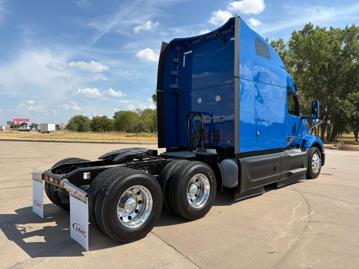Peterbilt 579 tractor unit in blue, side rear view showing a sleeper cab, dual rear axles, chrome wheels, and hitch area.