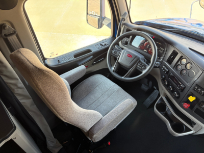 Peterbilt 579 truck cabin interior showing steering wheel and dashboard with gray fabric seats and control panels.