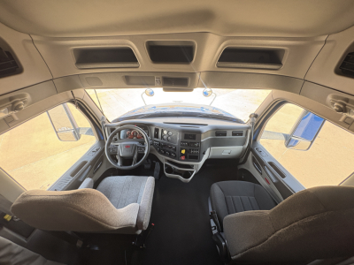 Peterbilt 579 cab interior view from entry, steering wheel, dashboard, and front seats visible through windshield.